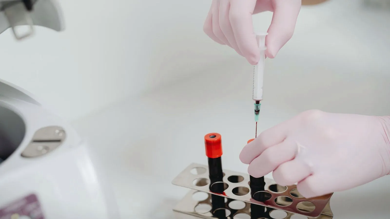 Gloved hands transferring a blood sample into tubes in a laboratory
