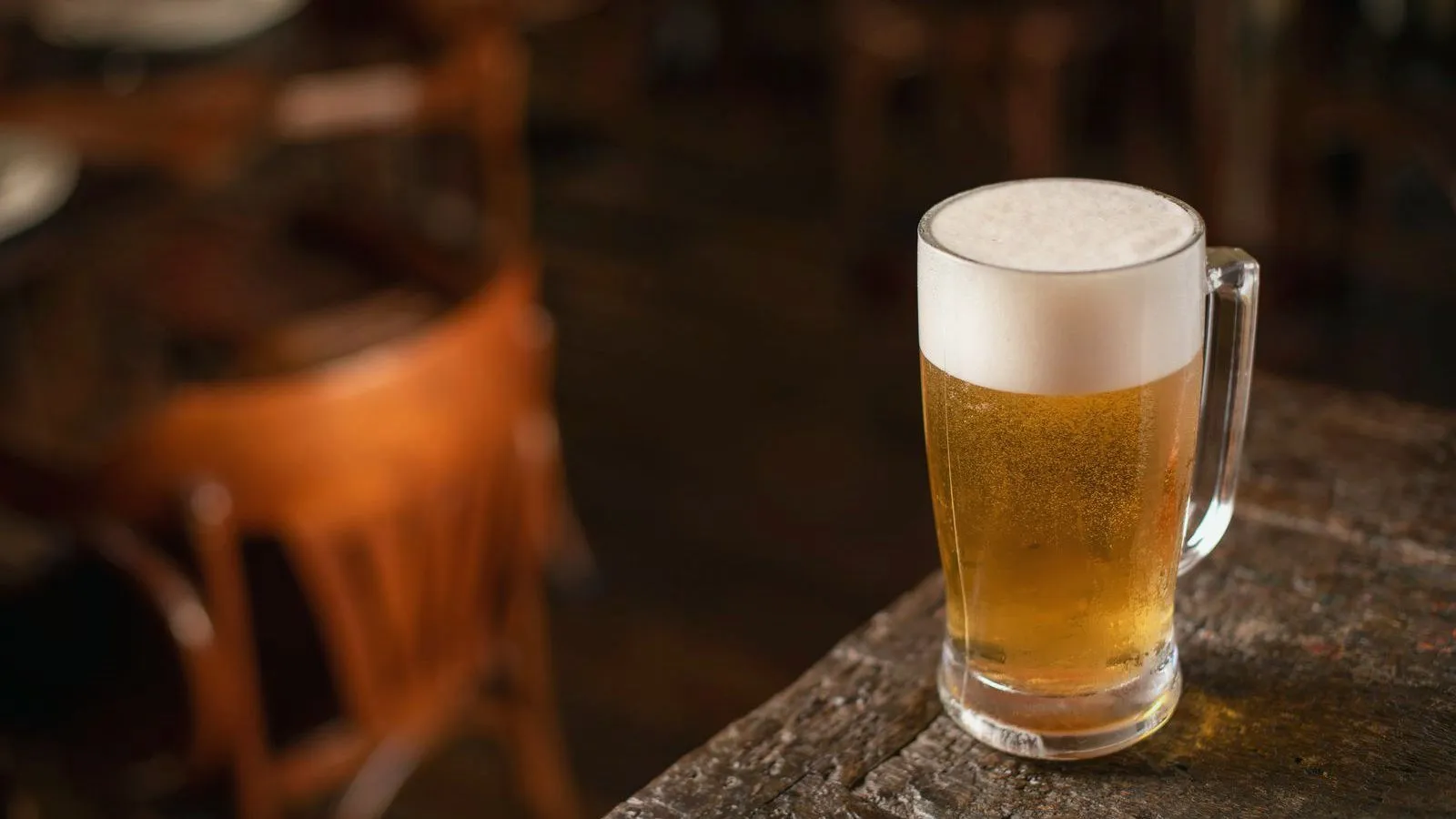 A glass mug of beer on a wooden table in an empty bar