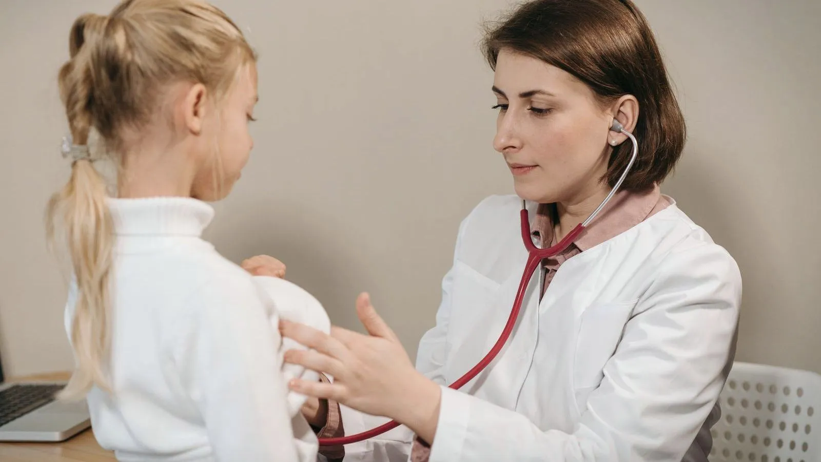 A doctor listening to a child's chest with a stethoscope at a desk
