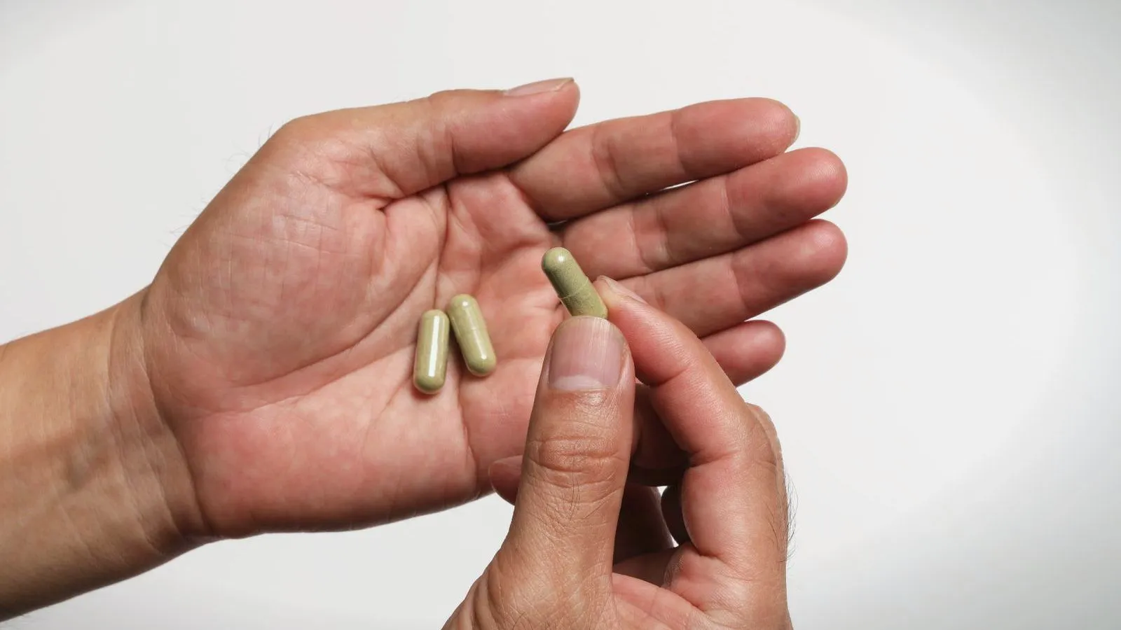 An open palm holding two green-beige capsules while the other hand picks up a third.
