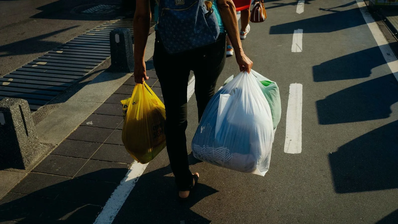 A person crossing a street carrying a small bag in one hand and a much larger one in the other