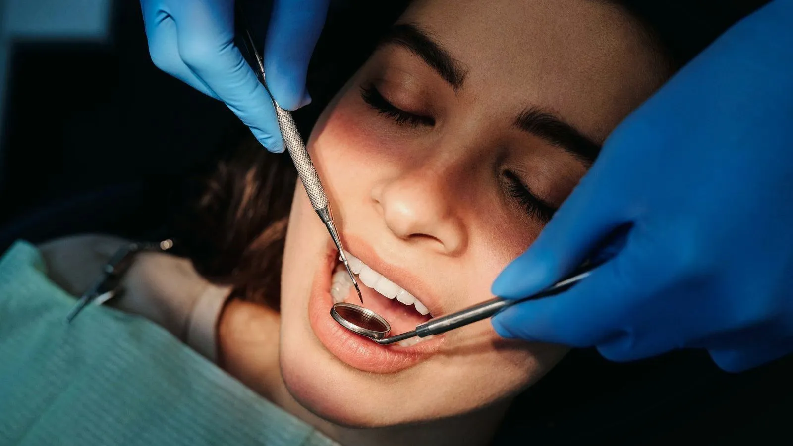 A dentist in blue gloves examining a patient's open mouth with a mirror and probe