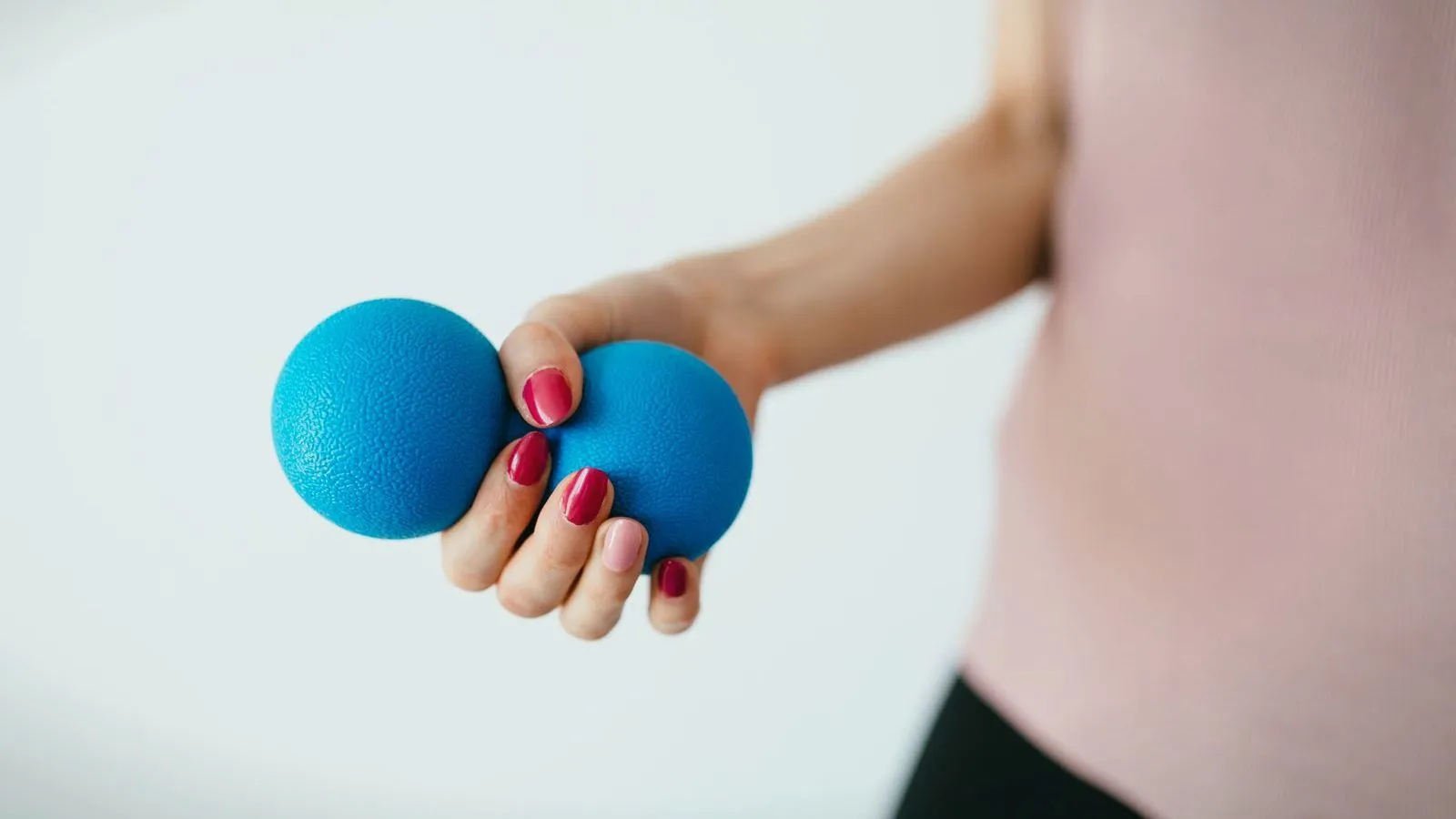 A hand squeezing two blue rubber grip balls against a white background