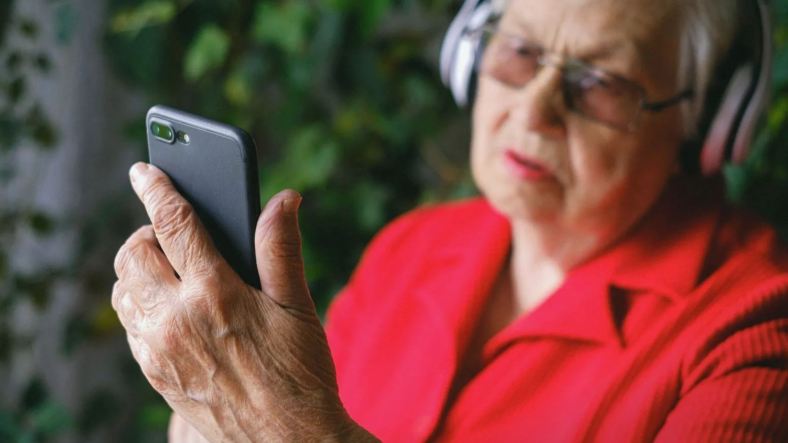 An older woman wearing headphones and looking at a phone screen