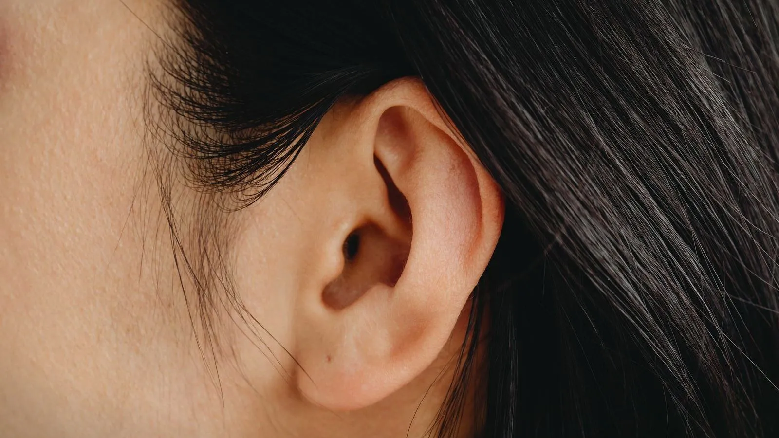 A close-up of a person's ear against dark hair