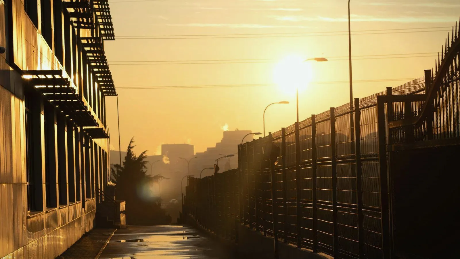 A low sun blazing through haze over a city street lined with railings