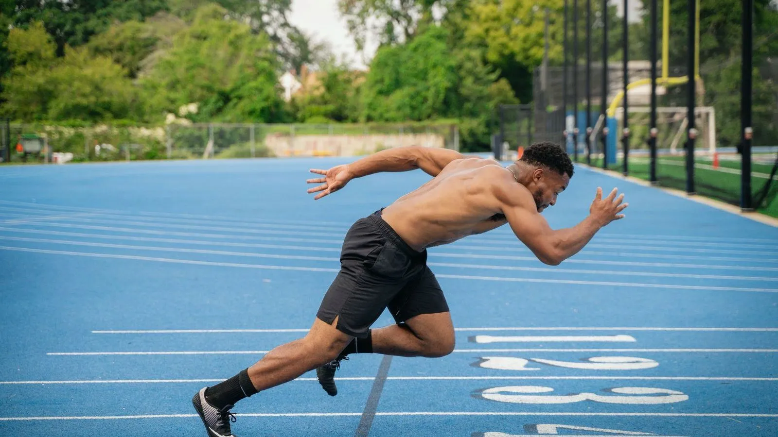 A man sprinting forward from a crouch on a blue running track.