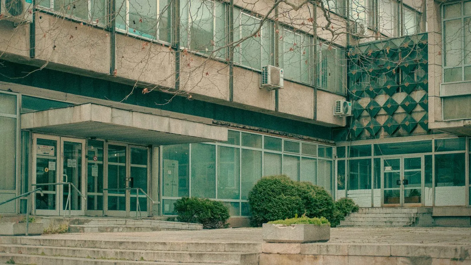 The glass entrance of an institutional building with steps and handrails