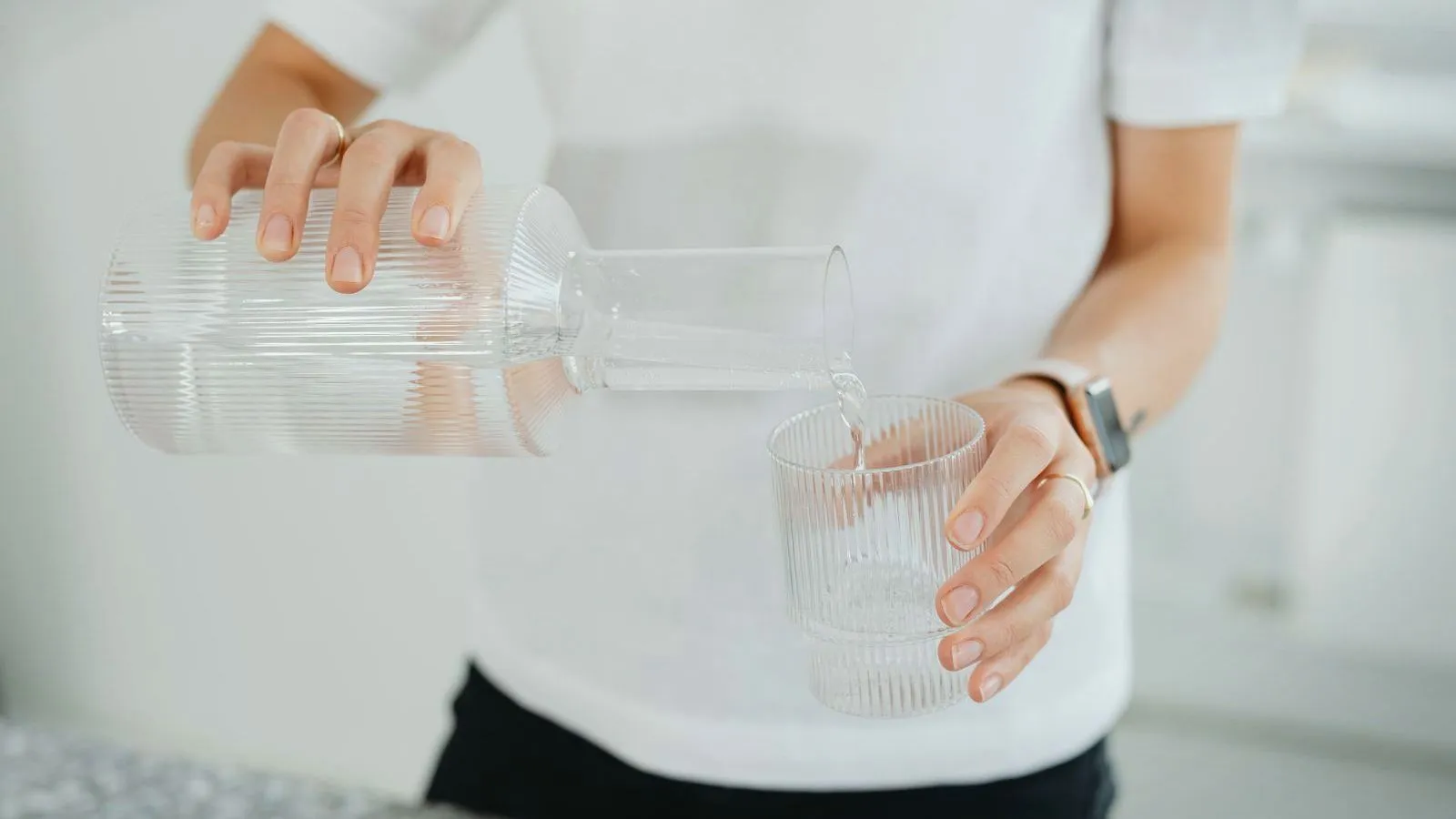 A person pouring water from a glass carafe into a ridged glass.