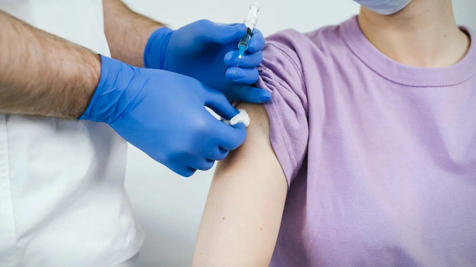 A gloved clinician giving an injection into a person's upper arm