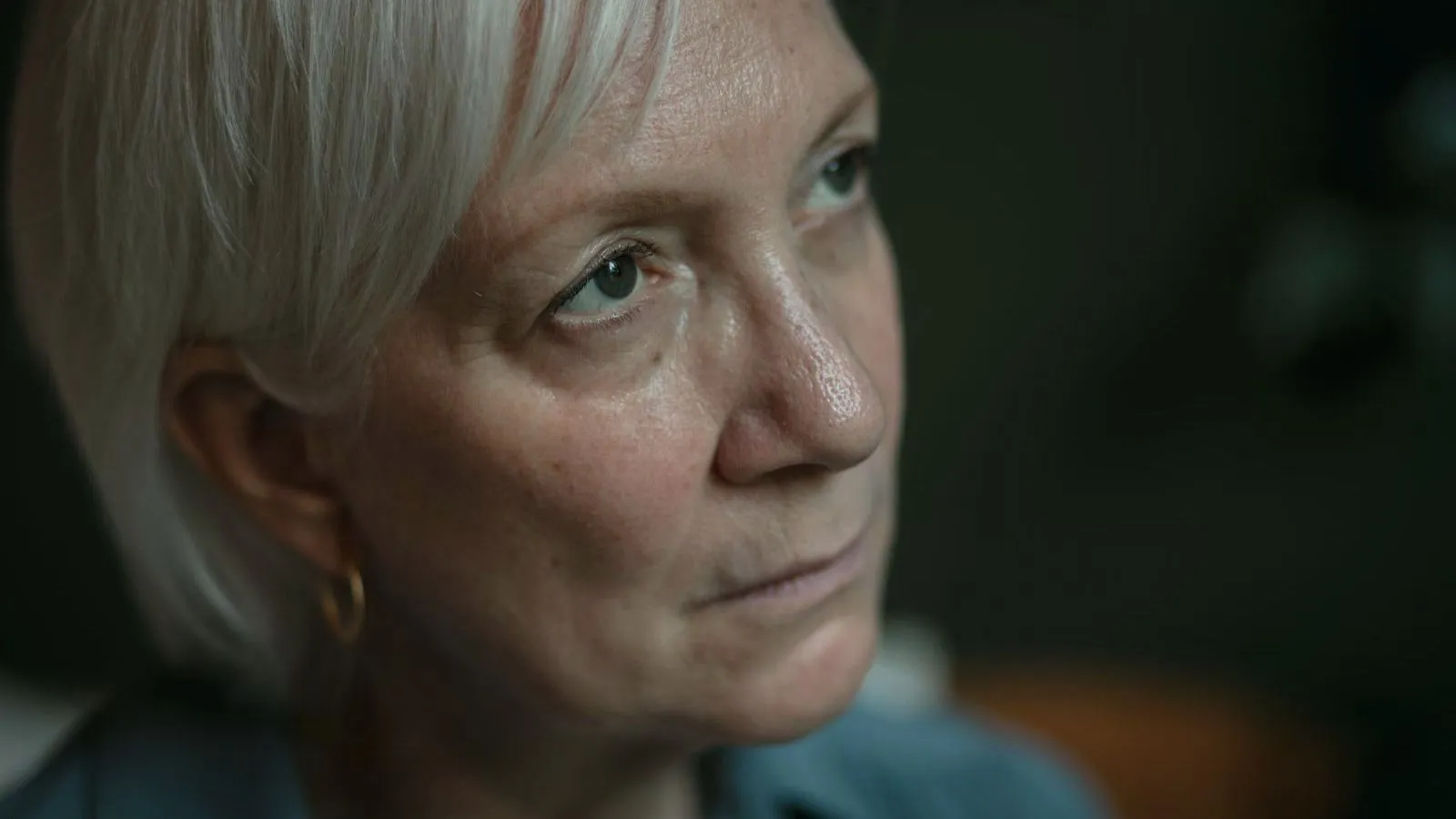 A close portrait of an older woman with short white hair looking away in low light