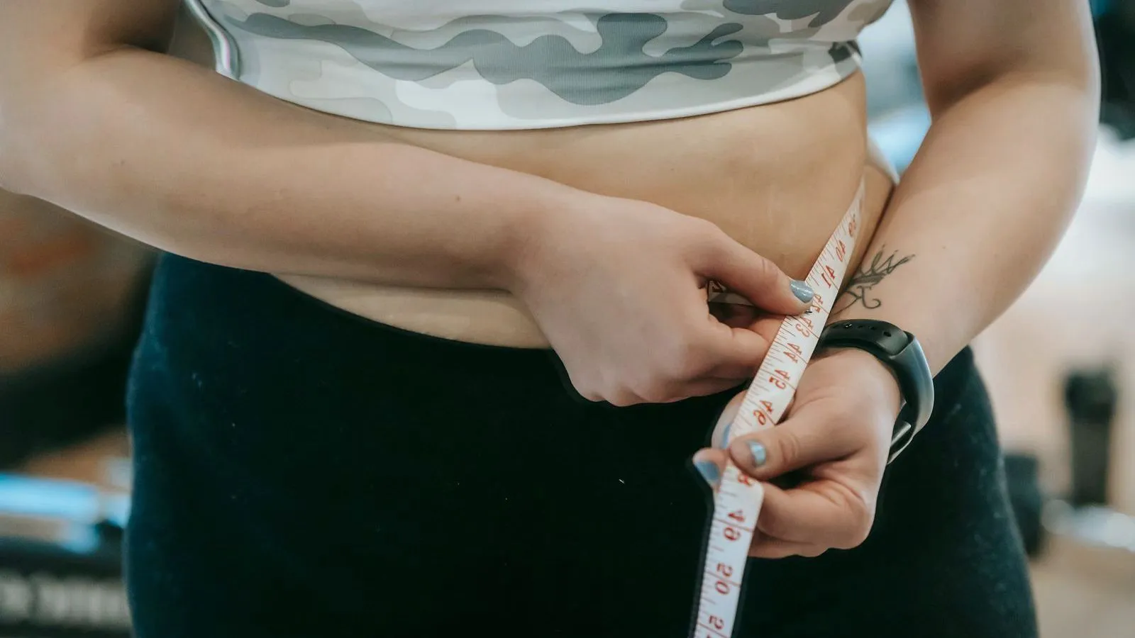 A person measuring their waist with a tape measure, shown close up