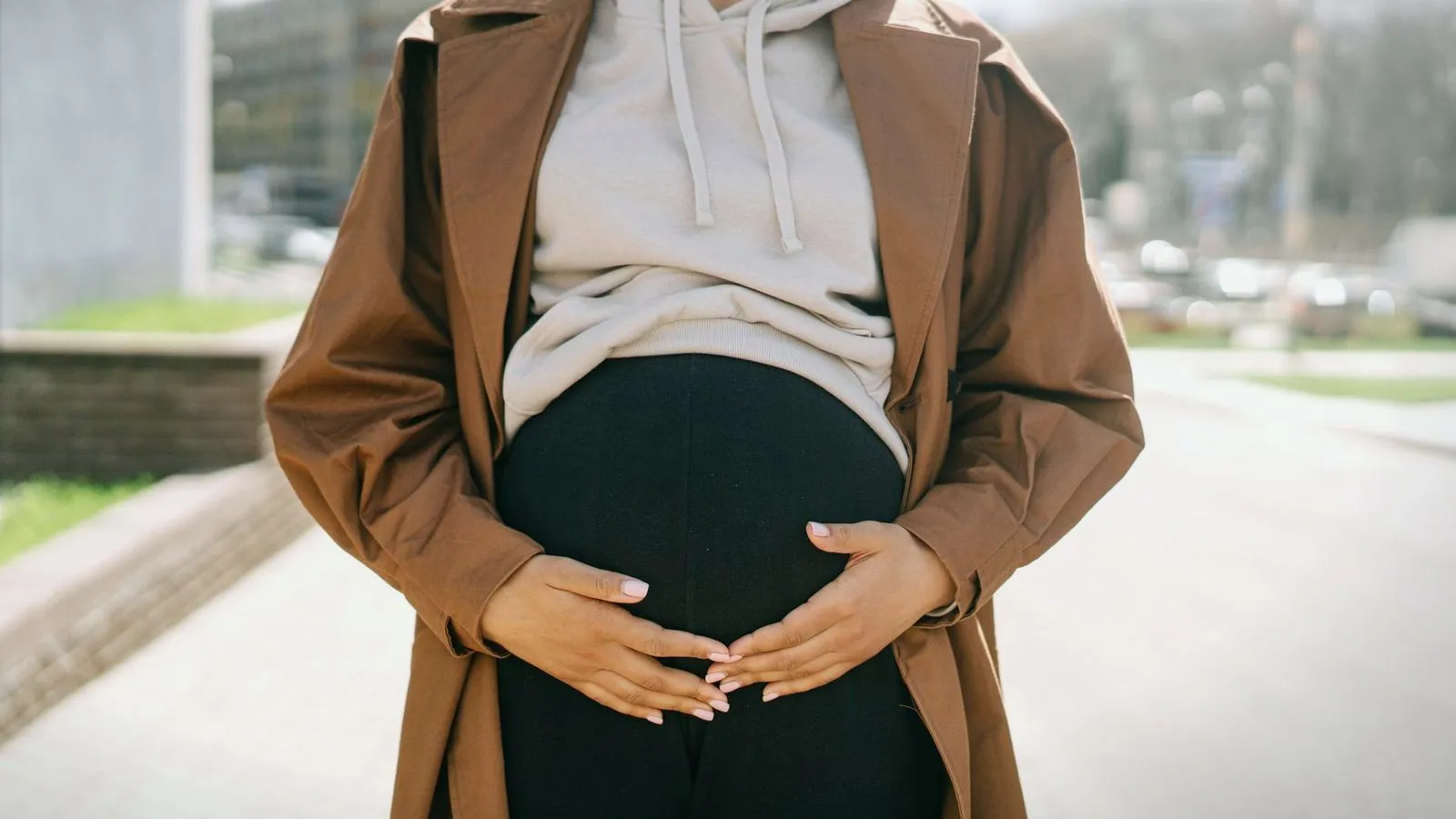 A pregnant woman in a coat resting both hands on her bump