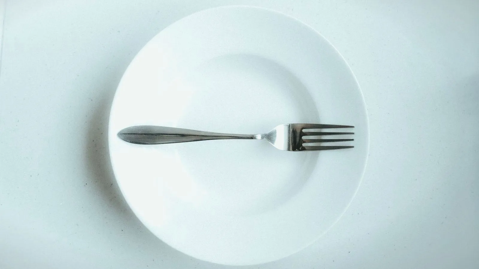 An empty white plate with a single fork on it.