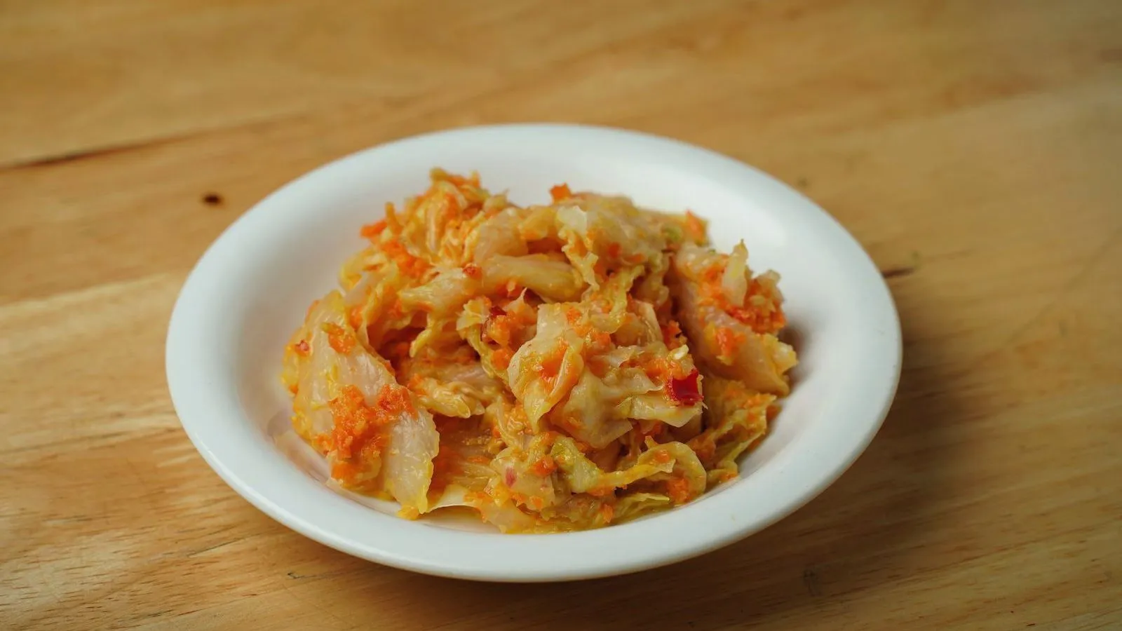 Kimchi served in a white bowl on a wooden table