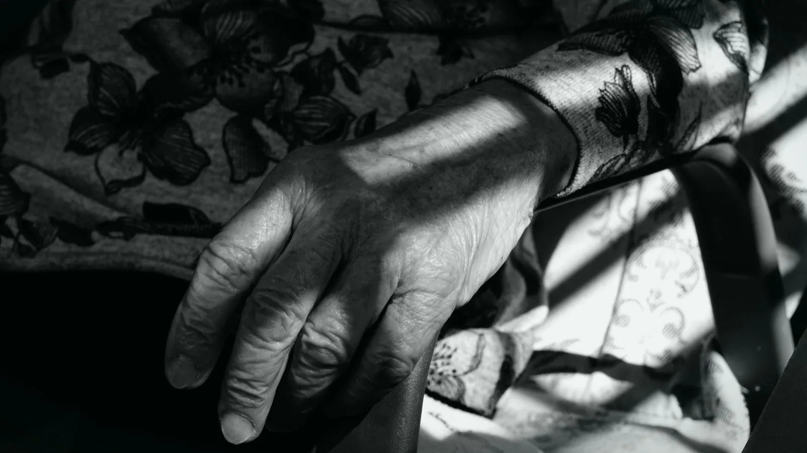 A black and white close-up of an elderly hand resting on a chair arm