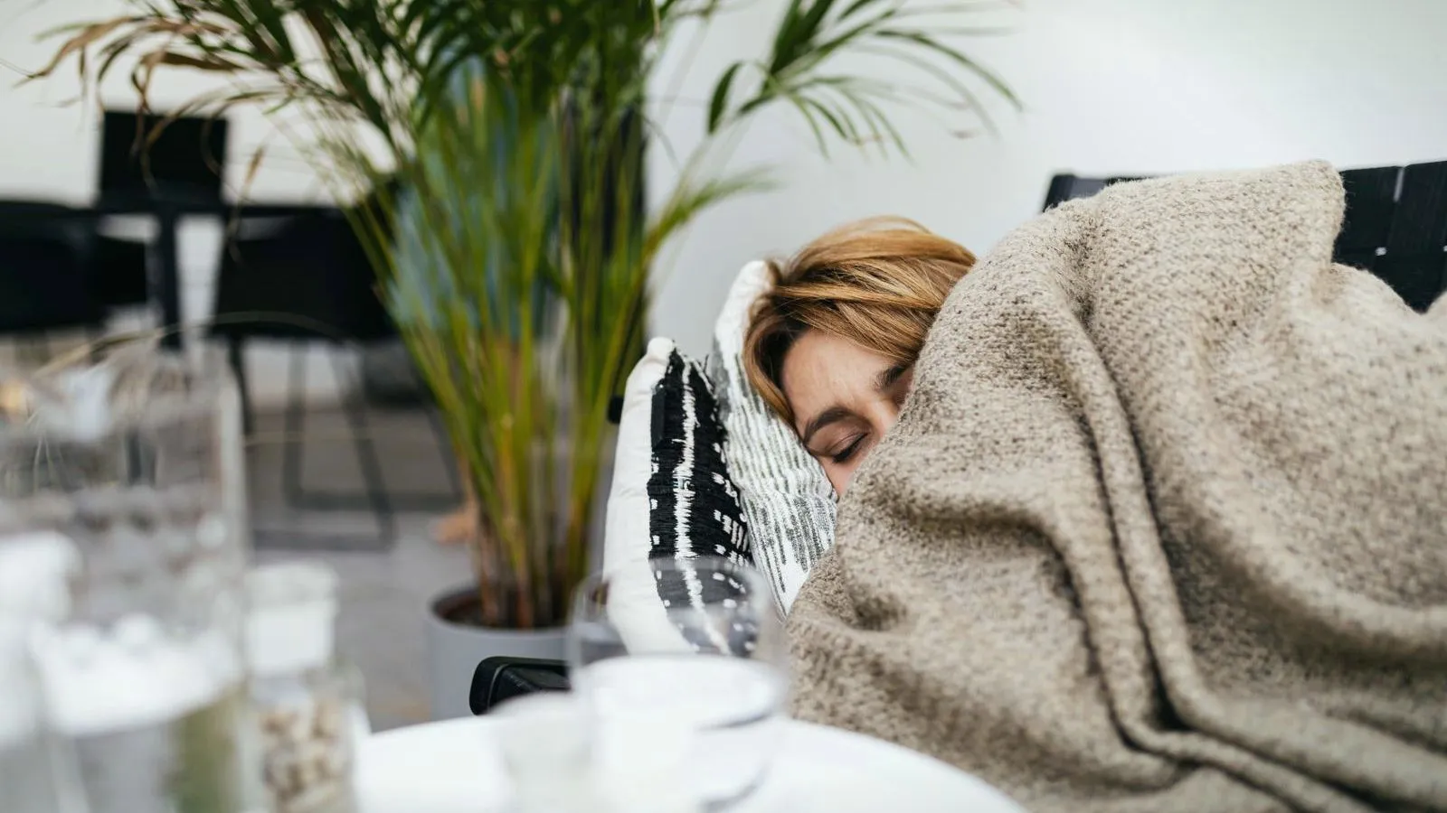 A person asleep under a blanket on a sofa in daylight