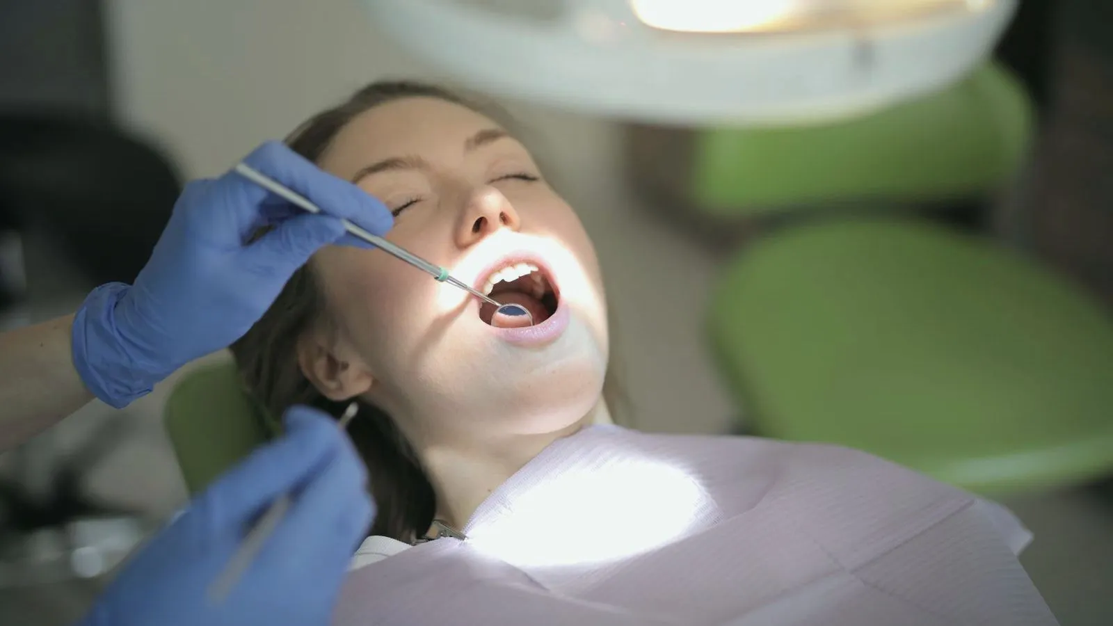 A dentist in blue gloves examining a patient's teeth with a mirror and probe