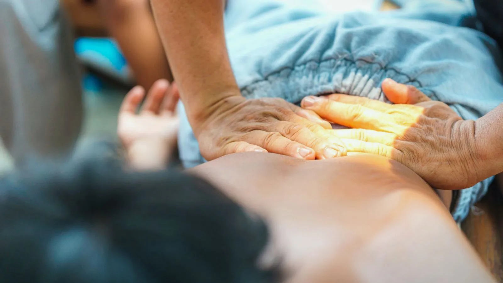 A therapist's hands pressing on the lower back of a person lying face down.