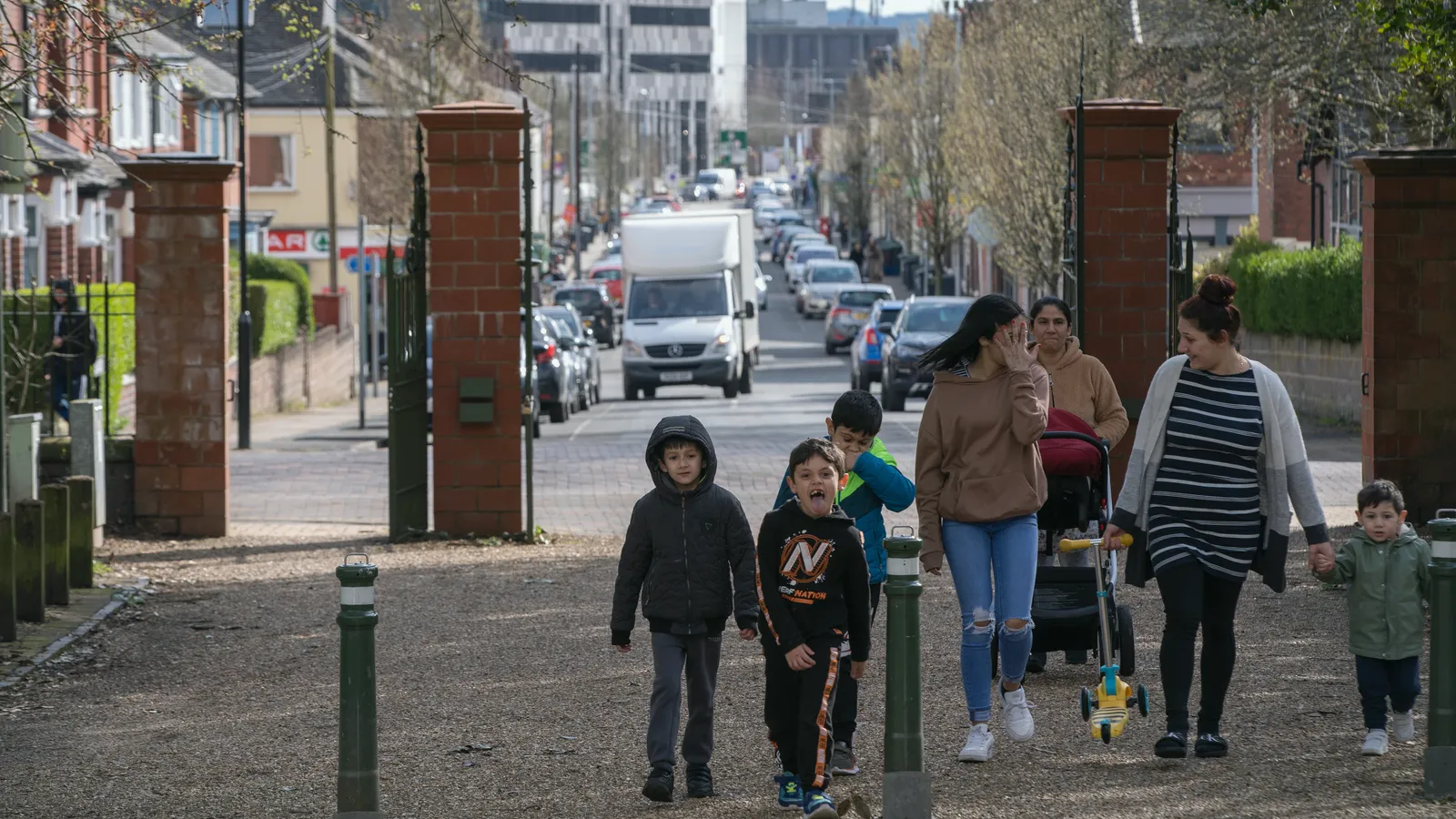 Children and adults walking along a residential street lined with parked cars