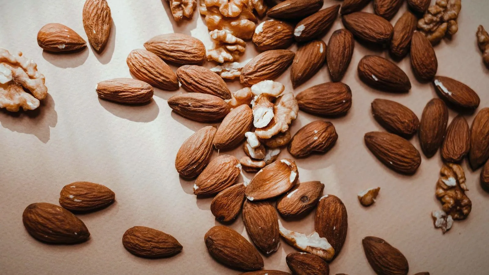 Almonds and walnut halves scattered across a pale surface
