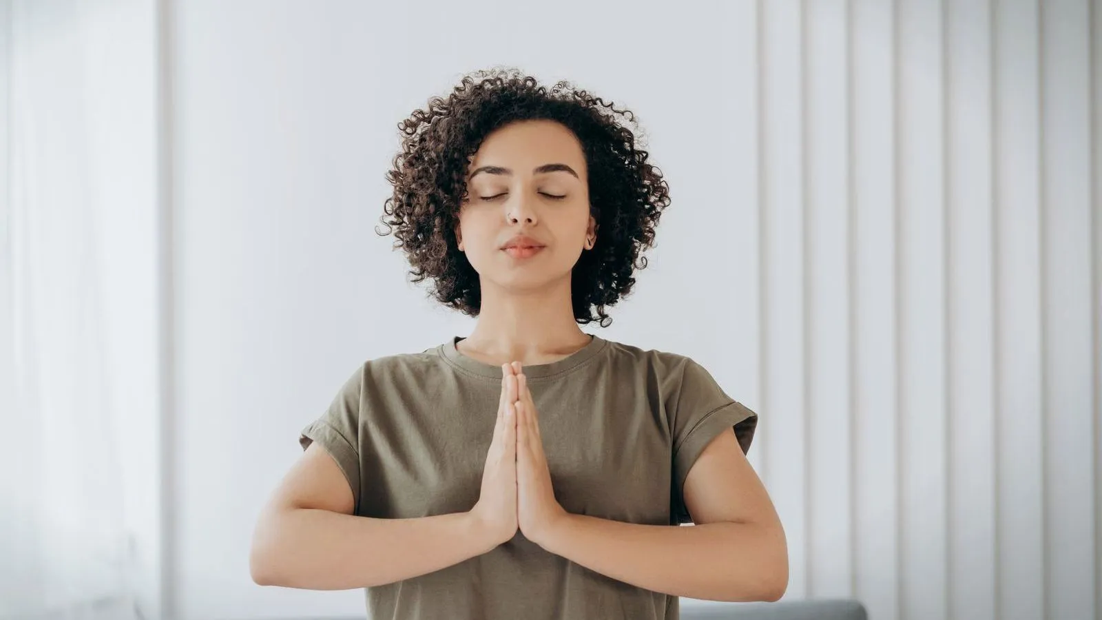 A woman meditating with her eyes closed and her palms pressed together.