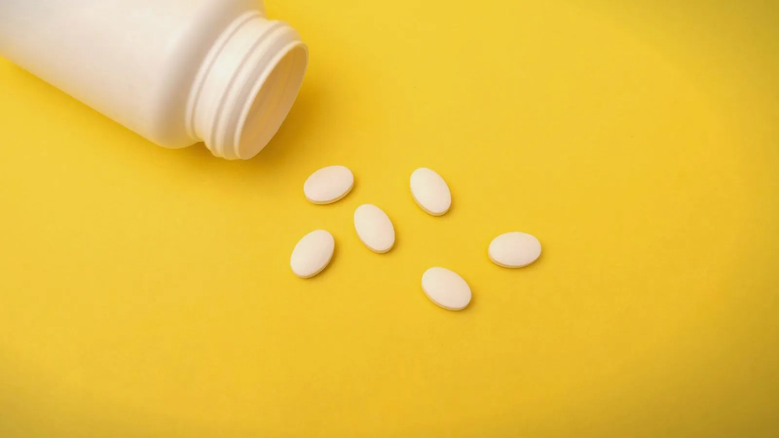 White tablets and an open bottle on a yellow background
