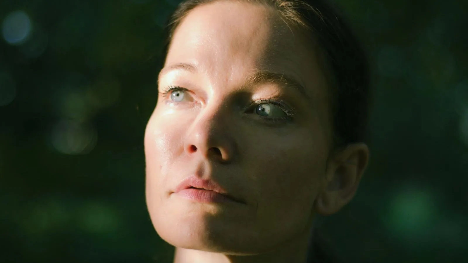A woman in her forties looking away, lit against a dark green background