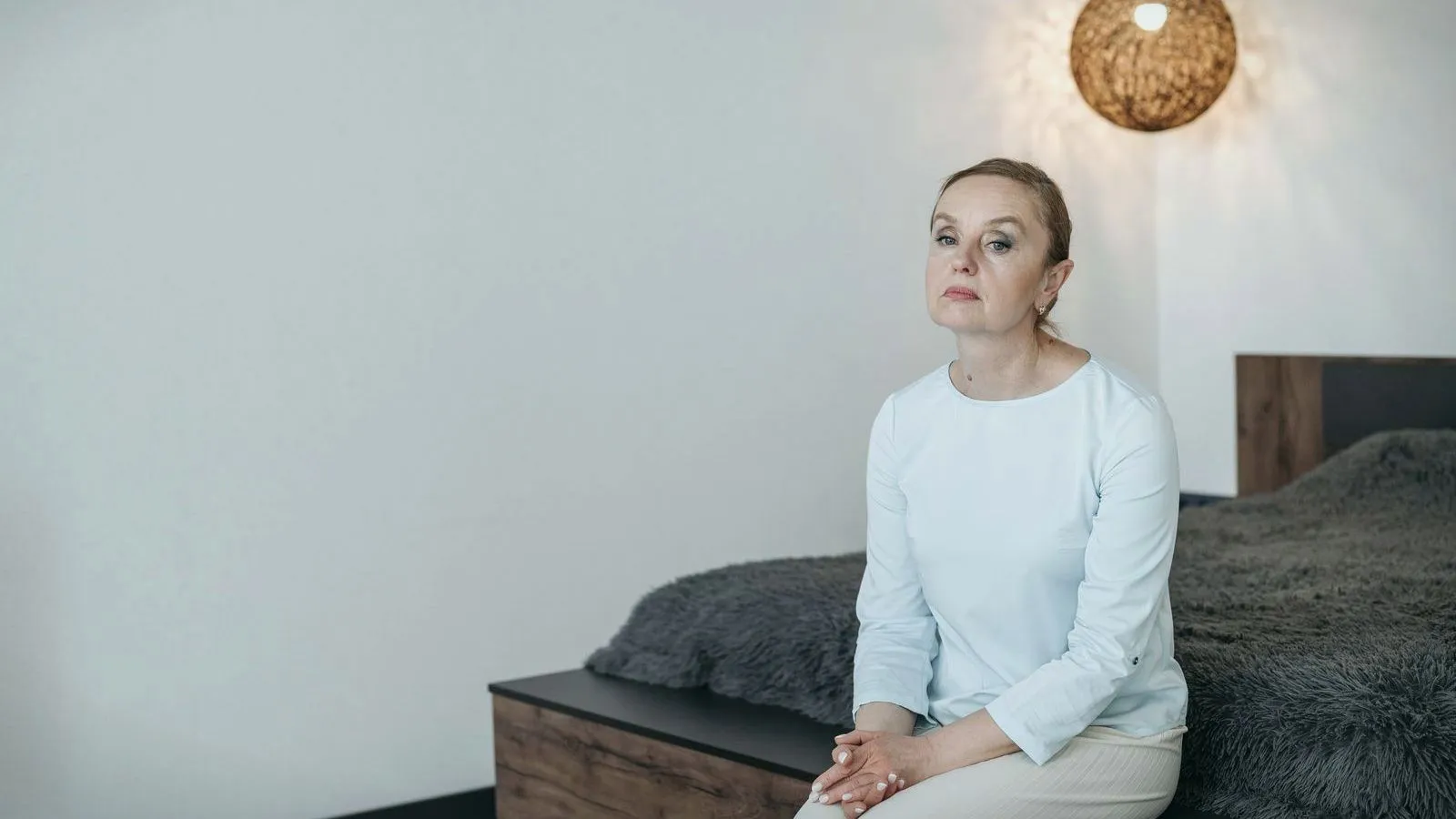 A middle-aged woman sitting on the edge of her bed