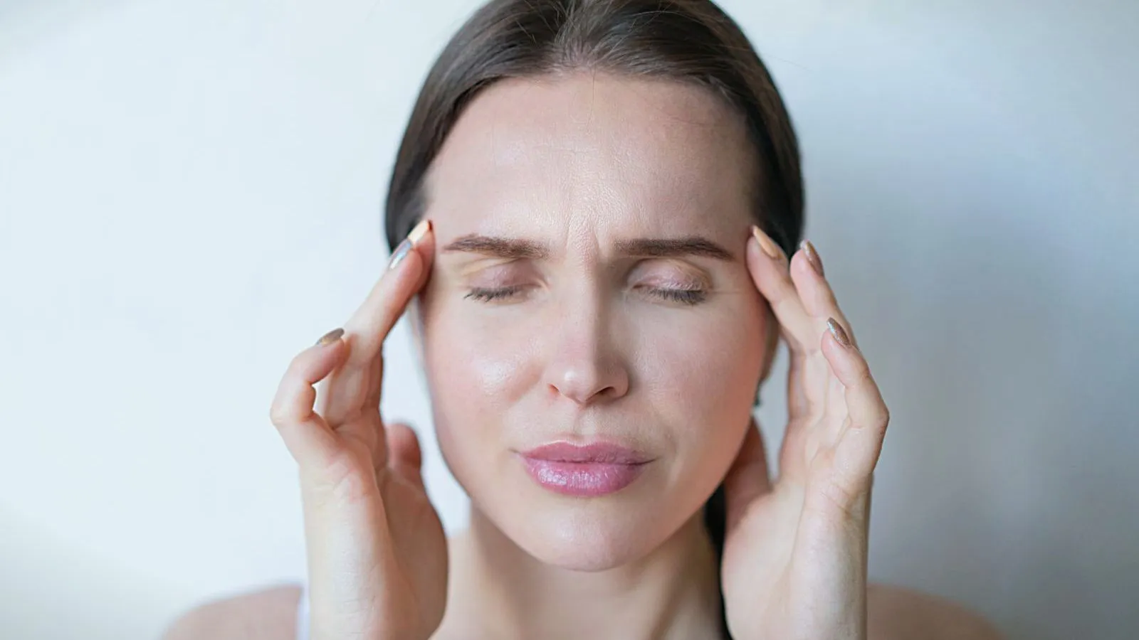 A person with eyes closed pressing their fingertips to their temples.