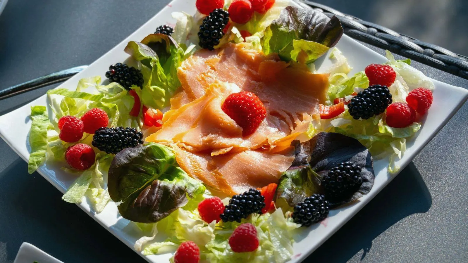 A square plate of smoked salmon on lettuce, topped with raspberries and blackberries.