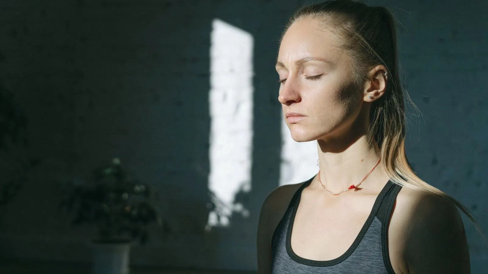 A woman in profile with her eyes closed in a dim room lit by a single window
