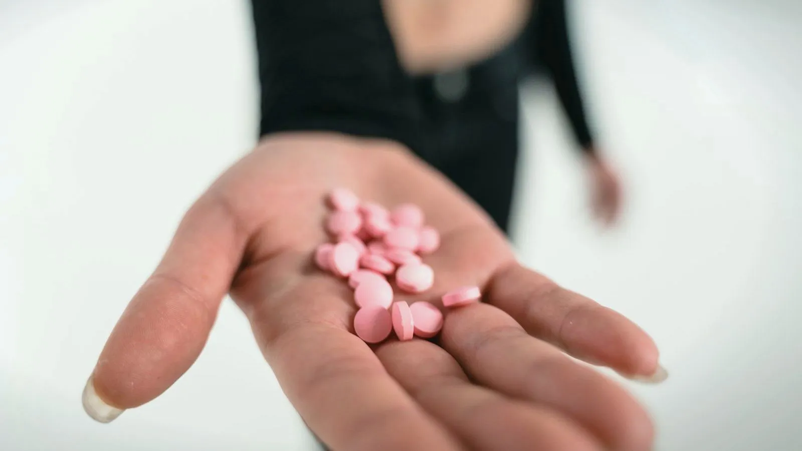 An open palm holding a small pile of round pink tablets.