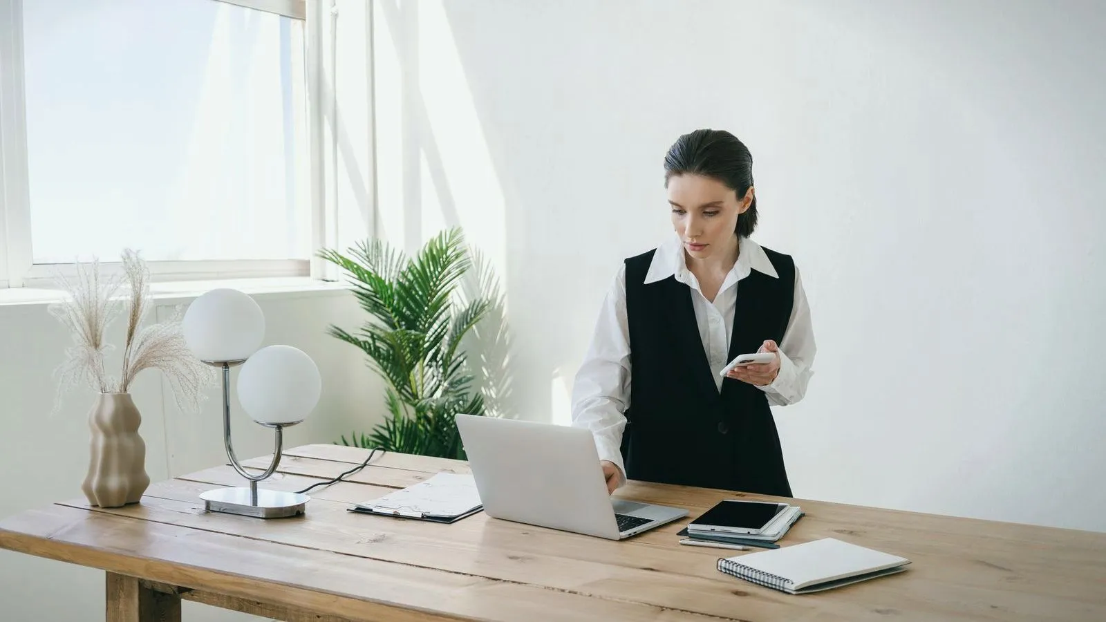 A woman working while standing at a desk beside a bright window