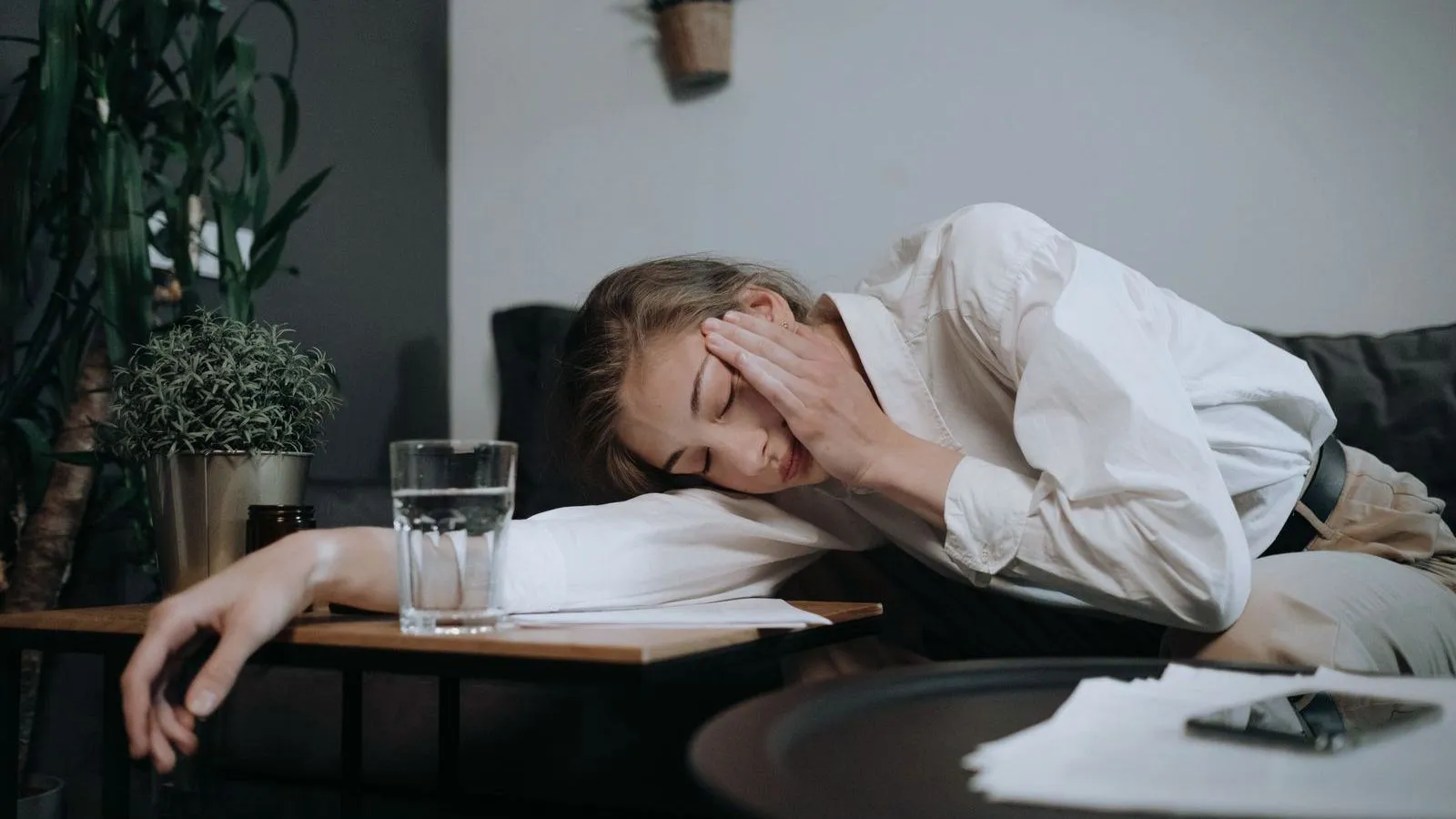 A young woman asleep with head resting on one arm beside a glass of water