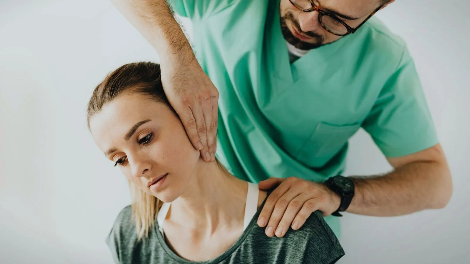 A clinician in scrubs with both hands supporting a woman's neck