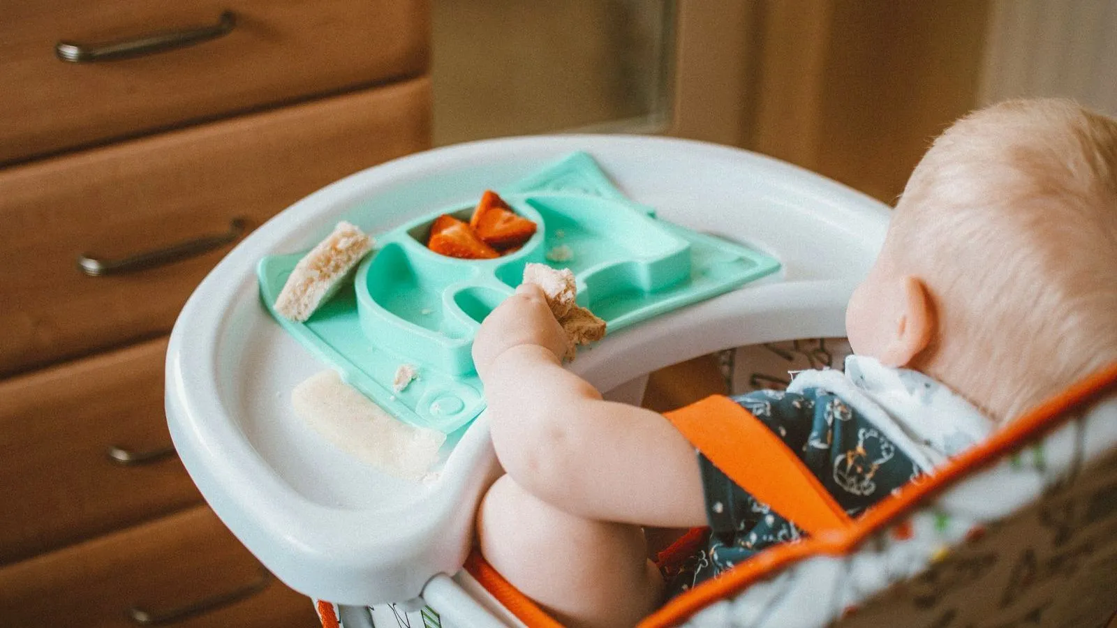 A toddler in a high chair reaching for food in a divided tray
