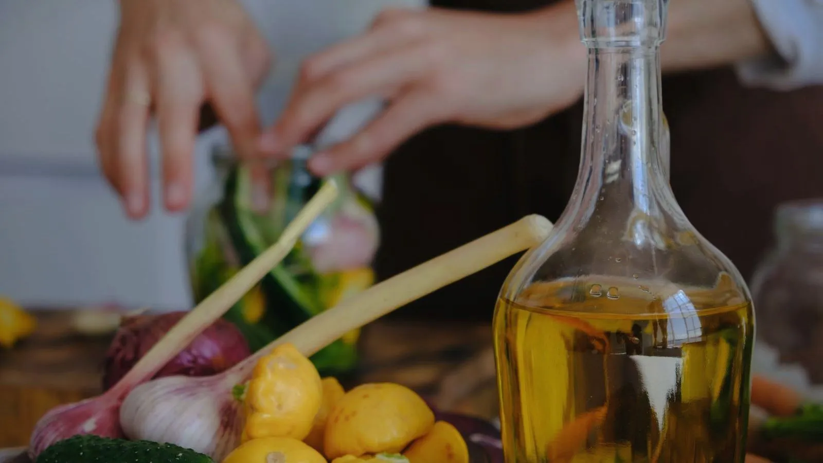 A clear glass bottle of oil beside garlic, lemongrass and vegetables being prepared.