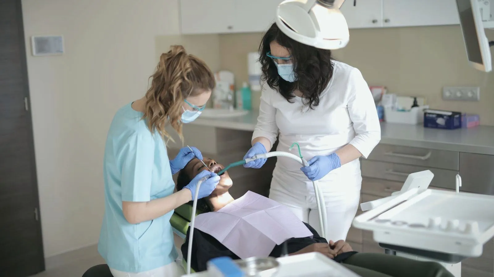 Two dental professionals treating a patient reclined in a dental chair.