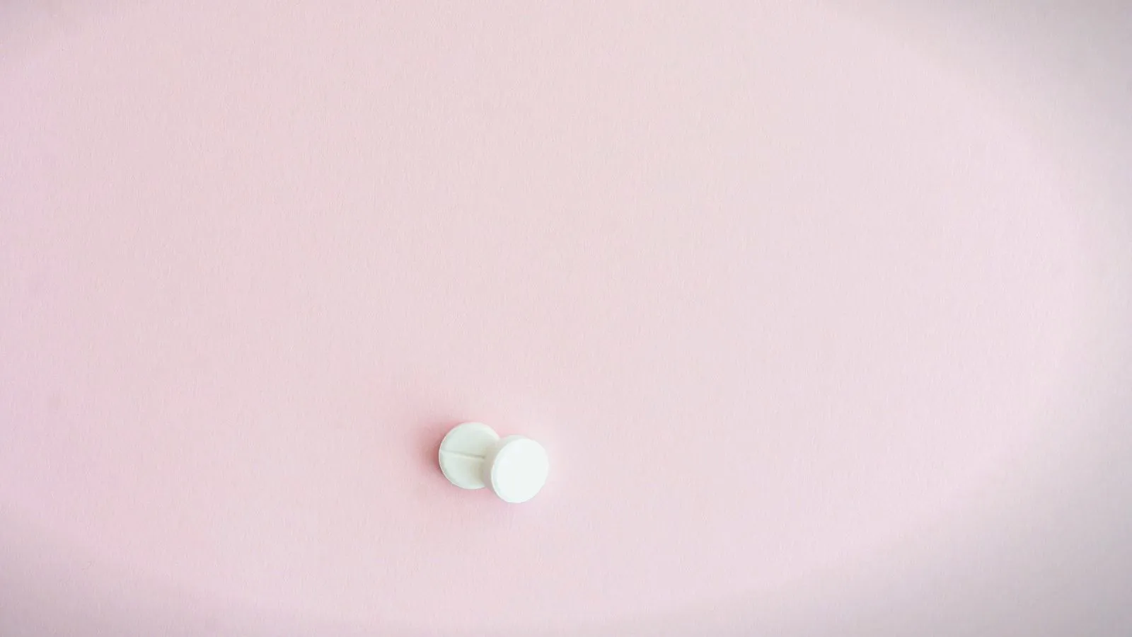 Two small white tablets on a plain pink background