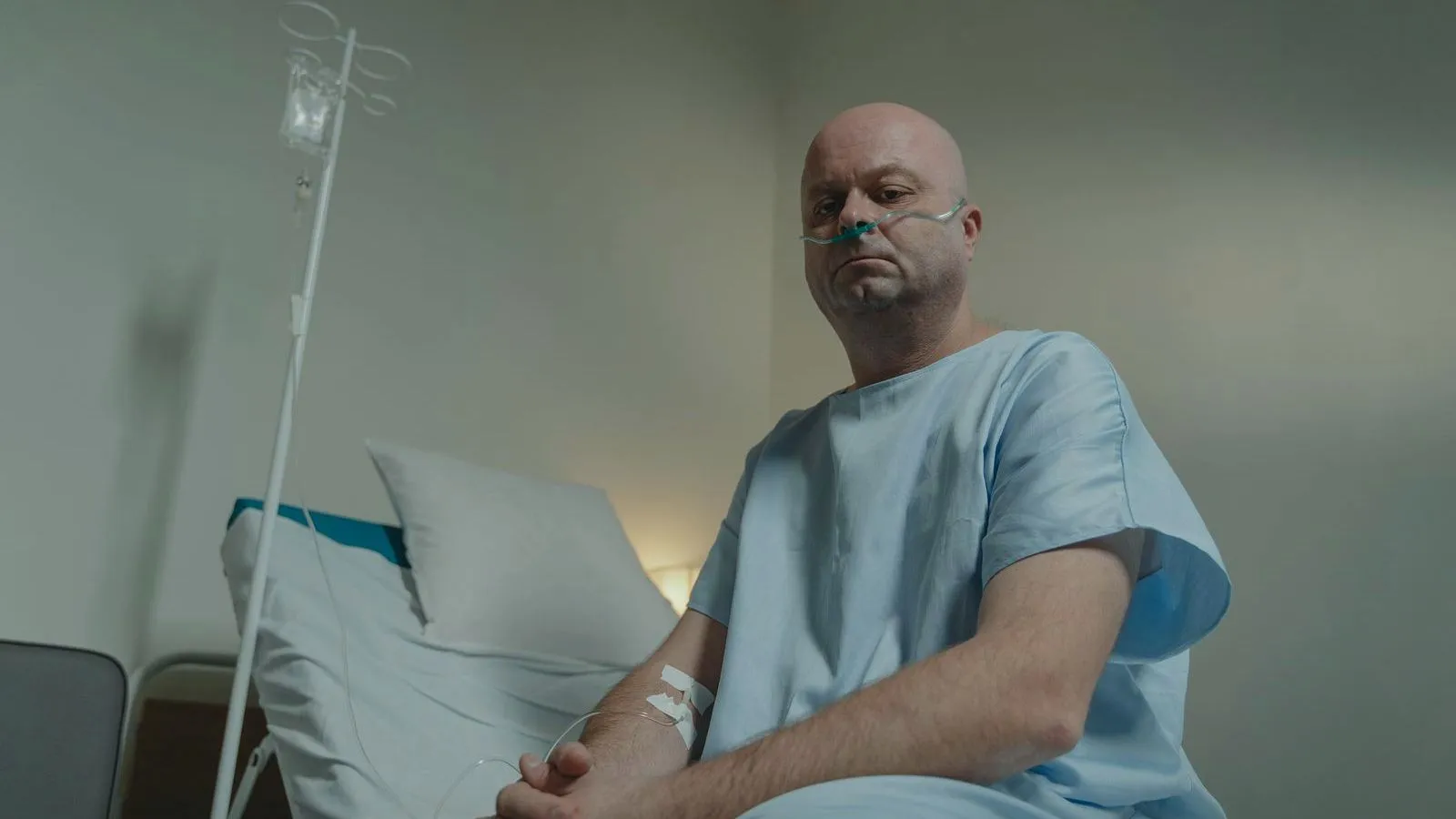 An older patient in a hospital gown sitting on the edge of a bed