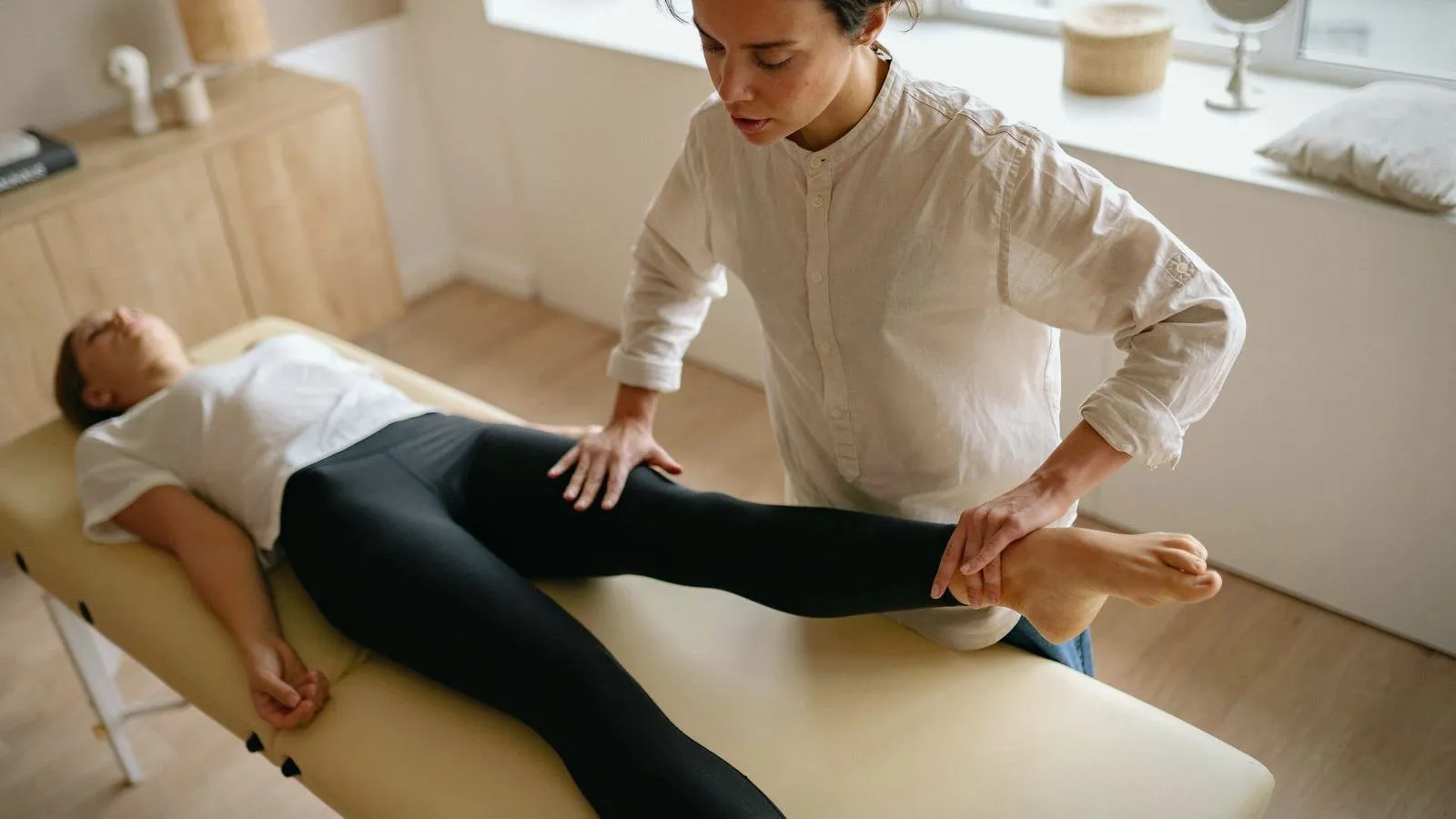 A physiotherapist in a white shirt holds the lower leg and foot of a person lying on a treatment table.