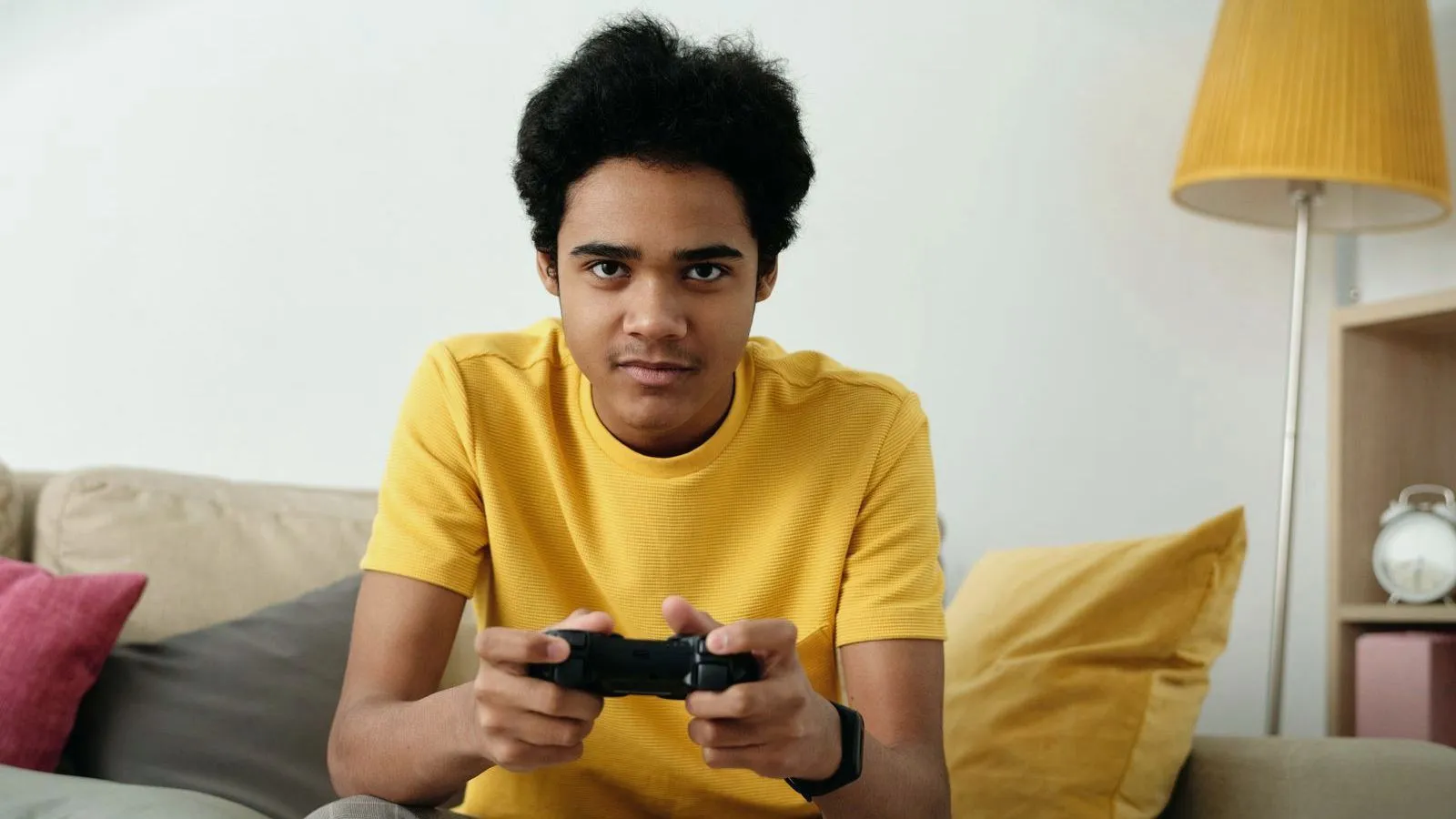A teenager in a yellow t-shirt holding a game controller, looking at the screen
