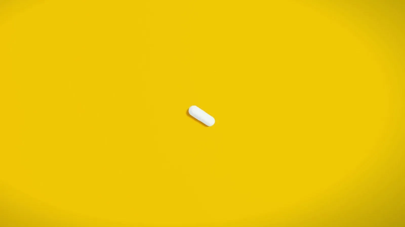 A single white capsule on a plain yellow background