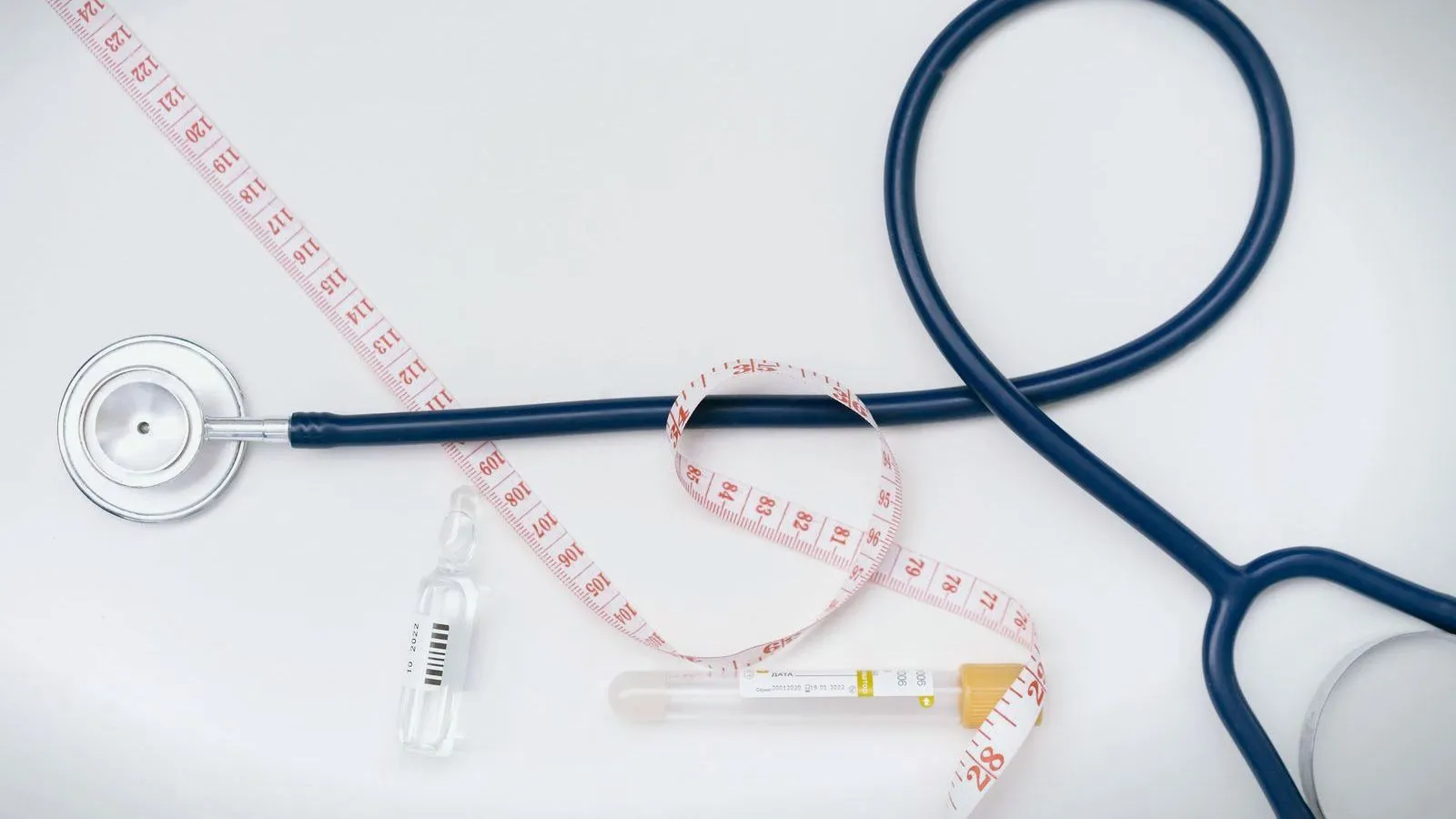 A stethoscope, a tape measure and small glass vials laid on a white surface