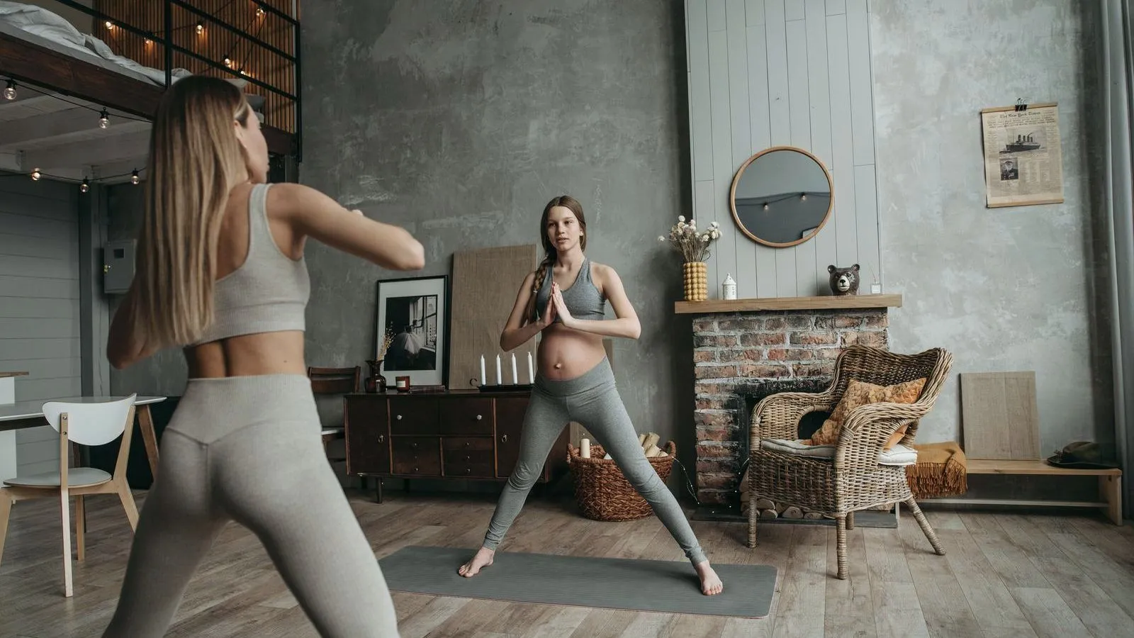 A pregnant woman holding a standing yoga pose while an instructor demonstrates in front of her