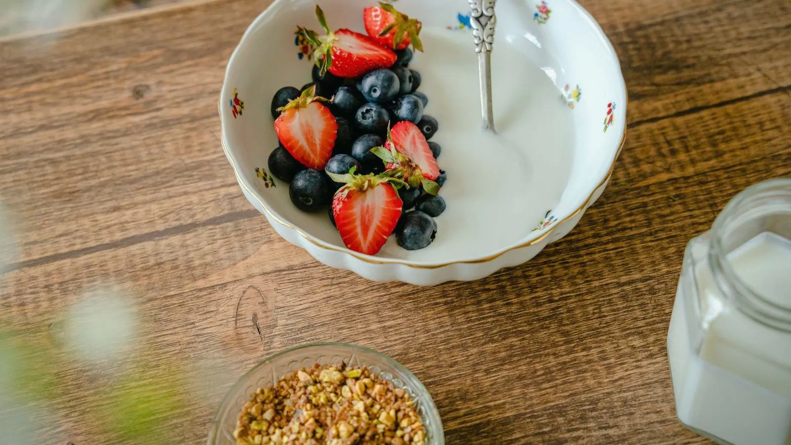 A bowl of plain yogurt with strawberries and blueberries on a wooden table