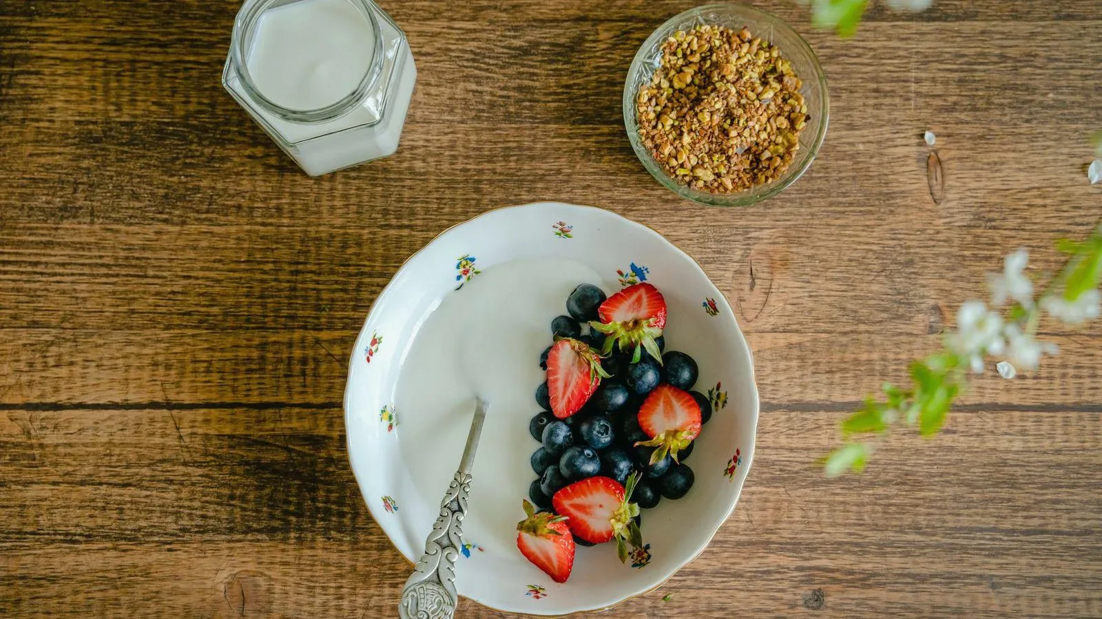 A bowl of yogurt topped with strawberries and blueberries on a wooden table
