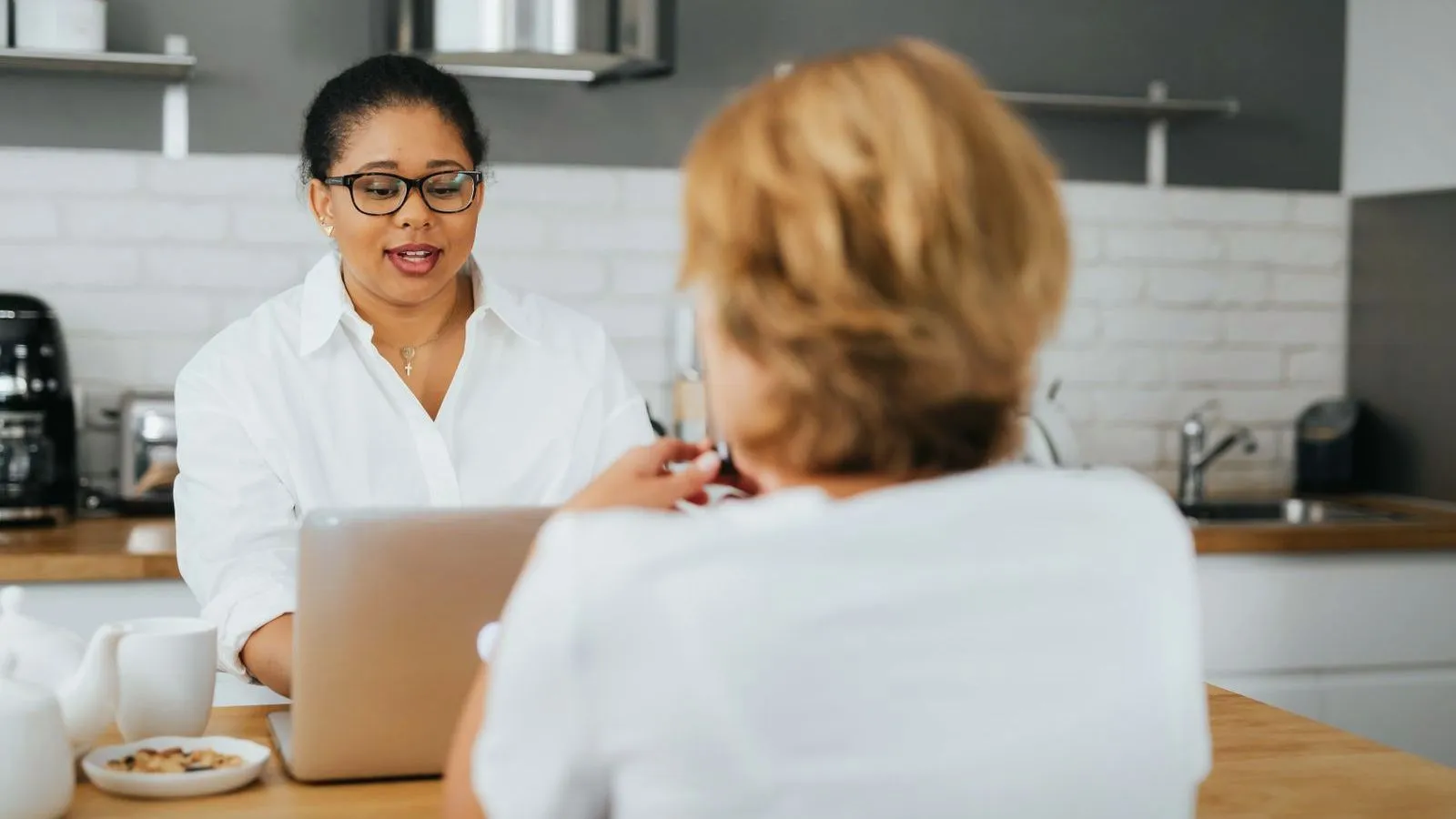 A dietitian with a laptop talking across a kitchen counter to an older woman seen from behind