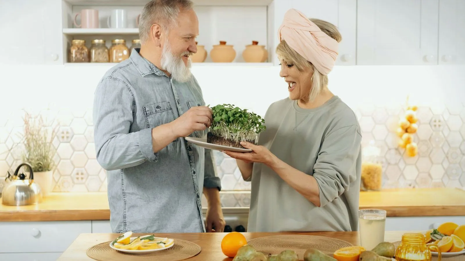 An older couple smiling as they share a tray of fresh microgreens in a bright kitchen